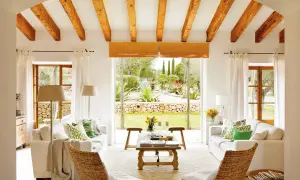 Salón con vigas de madera y vistas a un jardín exuberante, reflejo de la arquitectura mediterránea.