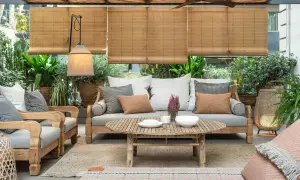 Acogedora terraza estilo mediterráneo con sofá, sillones de madera, mesa de centro y abundante vegetación.