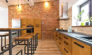 Cocina estilo industrial con pared de ladrillo visto, muebles de madera, encimera oscura y una isla con bancos.