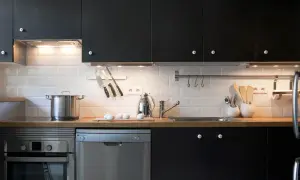 Cocinas en negro modernas con electrodomésticos de acero inoxidable, encimera de madera y azulejos blancos.