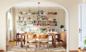 Comedor con decoración estilo nórdico, mesa de madera, sillas de diseño y estanterías blancas repletas de libros y objetos decorativos.