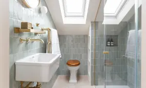 Elegantes mini aseos de cortesía con azulejos verde menta, lavabo blanco, ducha acristalada y luz cenital.