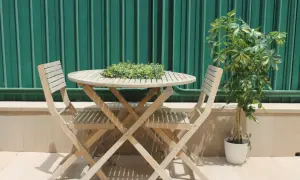 Mesa y sillas de madera en un rincón acogedor, ideal para disfrutar de terrazas con encanto. Una planta verde aporta vida.