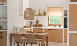 Cocina estilo mediterráneo con mesa de madera, sillas de mimbre y armarios de roble. Lámpara de mimbre y ventana con vistas a la vegetación.