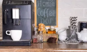 Máquina de café, taza, galletas y un letrero de "my Home Coffee bar" en un rincón de la cocina.