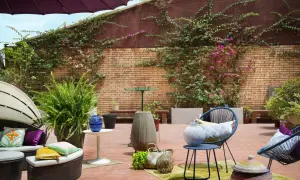 Acogedor **diseño terraza exterior** con muebles de ratán, sillas azules, plantas exuberantes y detalles decorativos en ladrillo.