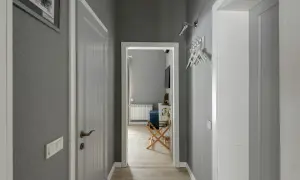 Pasillos con encanto, con paredes grises, puertas blancas y un cuadro en la pared. Se vislumbra una habitación con un radiador y un banco.