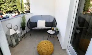 Acogedor rincón en unas terrazas pequeñas con encanto: sofá negro, cojines, mesa auxiliar con libro y plantas, y un puf amarillo.