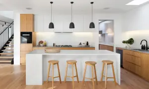Moderna cocina blanca y madera con isla central, taburetes de madera y escaleras de diseño.