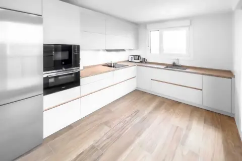 Cocina moderna con armarios blancos y encimeras de madera. Los suelos para cocinas blancas lucen un diseño de madera clara, aportando calidez al espacio.