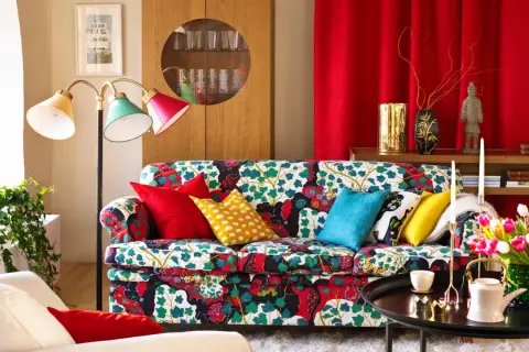 Sofá con estampado floral vibrante, cojines coloridos y una lámpara de pie que evoca un estilo vintage.