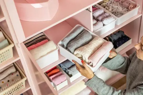 Una mujer organiza su armario, doblando ropa en contenedores. Aprende como ordenar un armario para tener todo a la vista y ordenado.