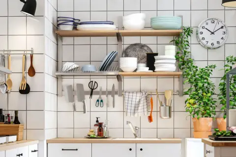 Una cocina pequeña y funcional con estantes llenos de vajilla, utensilios colgados y plantas verdes.