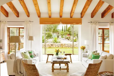 Salón con vigas de madera y vistas a un jardín exuberante, reflejo de la arquitectura mediterránea.
