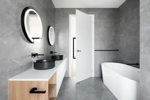 Elegante baño blanco y negro pequeño con lavabos negros, bañera exenta y espejos redondos iluminados.