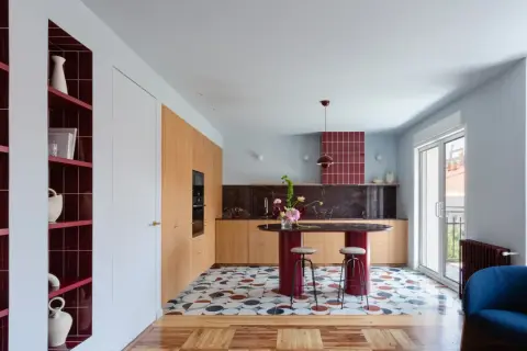 Cocina moderna con isla ovalada, estanterías rojas y suelo geométrico. Un ejemplo de **estudios interiorismo** audaces y coloridos.