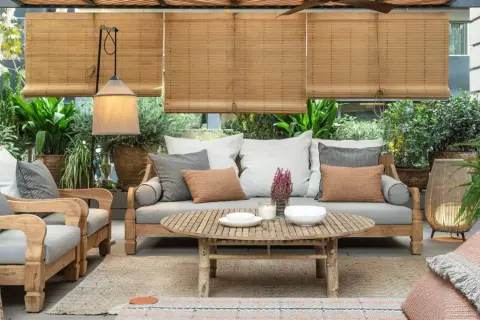 Acogedora terraza estilo mediterráneo con sofá, sillones de madera, mesa de centro y abundante vegetación.