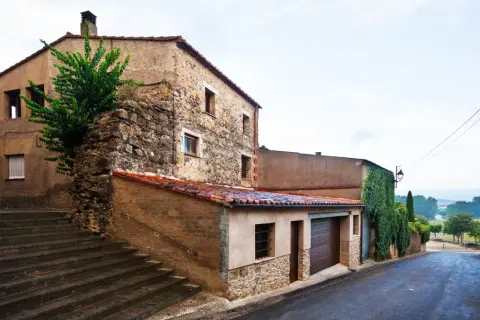 Escaleras de piedra suben hacia casas tradicionales de piedra y estuco, con tejados de teja roja. Una enredadera cubre parte de una pared.