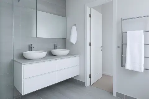 Modernos lavabos dobles sobre mueble blanco, espejo grande y azulejos grises. ¡Ideas para reformas de baños elegantes y funcionales!