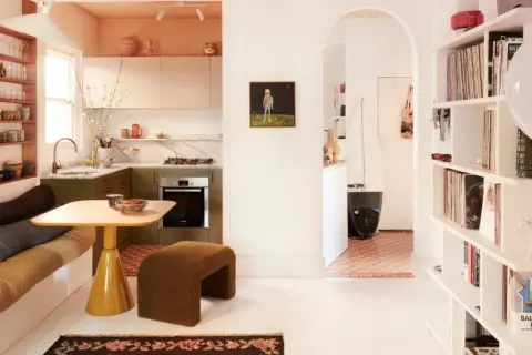 Acogedora casa pequena con cocina verde, sofá cama, mesa amarilla y estanterías llenas de objetos.
