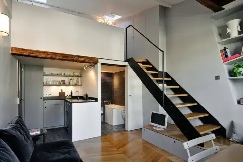 Moderno loft con altillo. Escalera metálica negra, cocina compacta y baño con azulejos. Ideas para espacios pequeños.