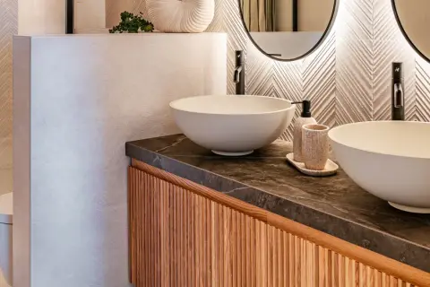 Modernos cuartos de baños con lavabos sobre encimera, grifería negra y detalles en madera.