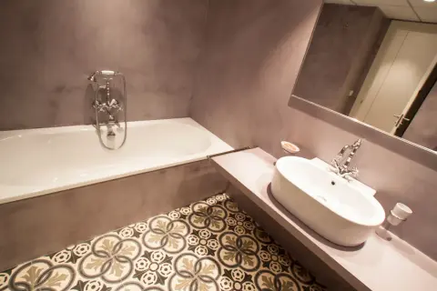 Baño moderno con microcemento en paredes y suelo de baldosas hidráulicas. Bañera y lavabo de diseño.