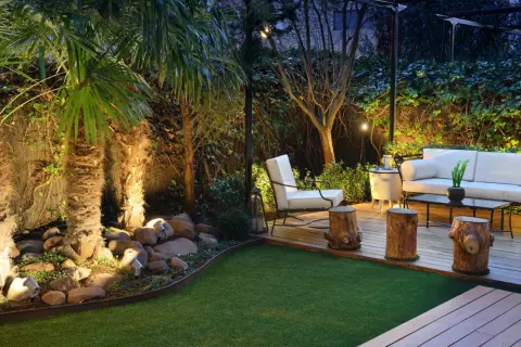 Jardines pequeños y sencillos con palmeras iluminadas, césped artificial y mobiliario de exterior.