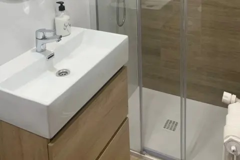 Moderno lavabo sobre mueble de madera, ducha con mampara y azulejos imitación madera. ¡Renovar baño sin obra es posible!