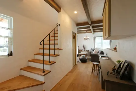 Un acogedor aseo bajo escalera con escalones de madera y barandilla negra. La sala de estar rústica se abre al fondo.
