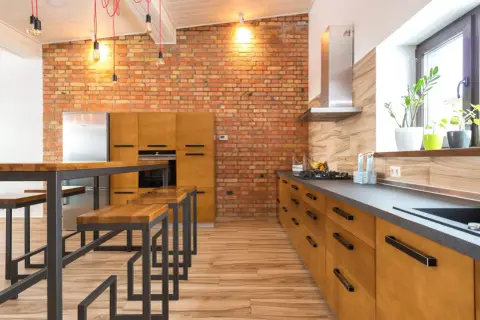 Cocina estilo industrial con pared de ladrillo visto, muebles de madera, encimera oscura y una isla con bancos.