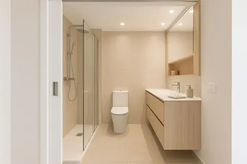 Un elegante cuarto de baño moderno con ducha de cristal, inodoro y mueble de lavabo de madera clara.