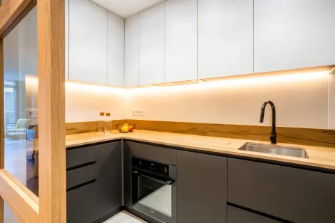 Cocinas negras y madera, con encimera de madera clara, armarios superiores blancos y detalles modernos.