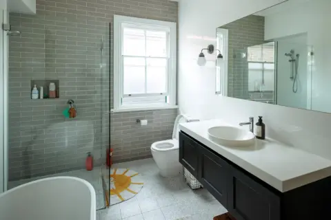 Baño moderno con ducha sin mampara, bañera exenta, lavabo sobre encimera y WC. Azulejos grises y suelo estampado.