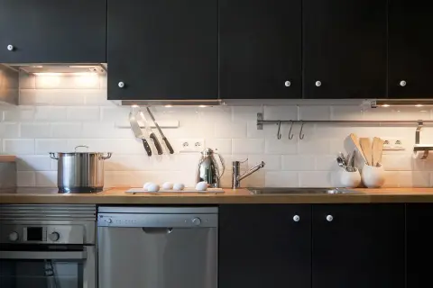 Cocinas en negro modernas con electrodomésticos de acero inoxidable, encimera de madera y azulejos blancos.