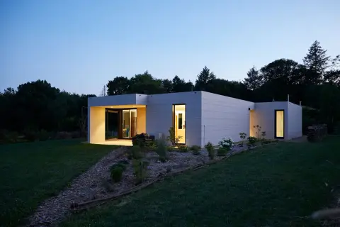 Modernos modelos de casas unifamiliares con fachadas de baldosas grises, iluminadas al anochecer.