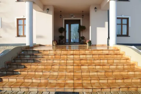 Amplias escaleras de entrada a un chalet, con escalones de baldosas naranjas que brillan bajo el sol.