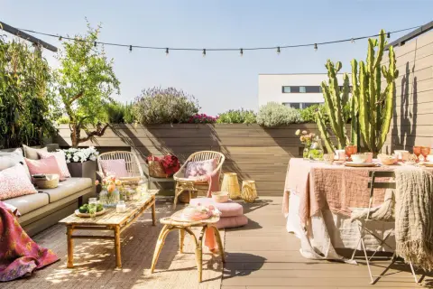 Terraza de ático lista para disfrutar. Una reforma que invita a la relajación con mobiliario de ratán, textiles suaves y plantas exuberantes.
