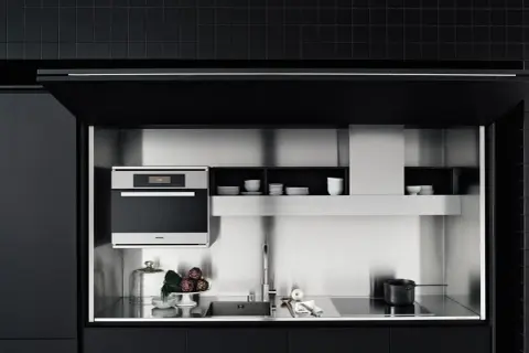 Cocinas invisibles: un horno Miele, fregadero y placa de inducción integrados en un diseño minimalista de acero inoxidable y gabinetes negros.