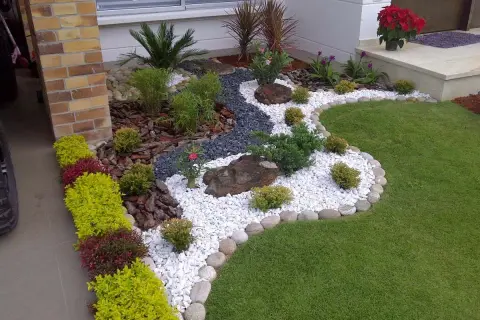 Un jardín moderno con grava blanca, rocas, plantas verdes y flores rojas, diseñado por paisajistas de jardines.