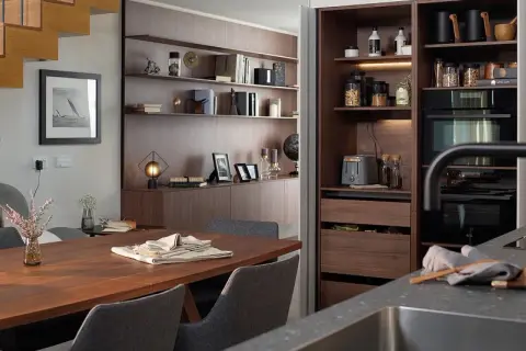 Comedor y zona desayuno cocina con mesa de madera, sillas grises y estanterías empotradas.