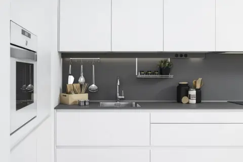 Moderna cocina blanca y gris con electrodomésticos integrados, fregadero de acero inoxidable y utensilios de cocina colgados.