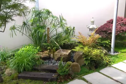 Un sereno mini jardín japonés en casa, con cascada de agua, rocas, plantas exuberantes y una linterna de piedra.