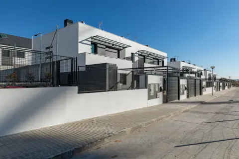 Modernos chalets adosados blancos con vallas metálicas y puertas de garaje.