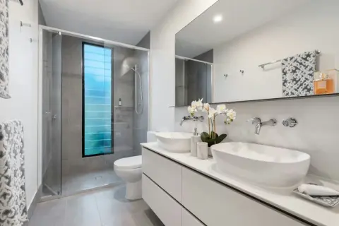 Elegantes baños modernos con ducha, lavabos dobles y ventana azul.