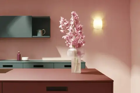 Elegante cocina rosa con encimeras de color burdeos, armarios verde azulado y un ramo de flores rosas.
