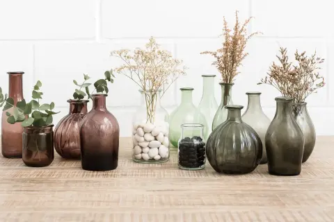 Variedad de jarrones de cristal grandes, algunos con ramas secas y hojas verdes, perfectos para decorar.
