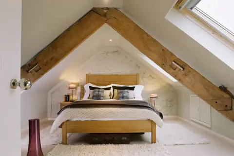 Dormitorio acogedor bajo un tejado con vigas de madera expuestas, ideal para levantar tejado para hacer buhardilla.