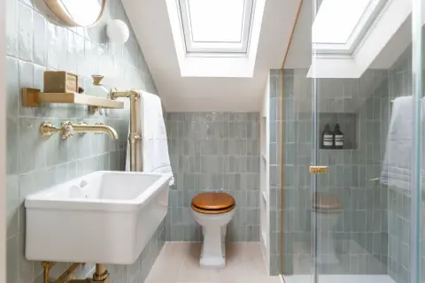 Elegantes mini aseos de cortesía con azulejos verde menta, lavabo blanco, ducha acristalada y luz cenital.