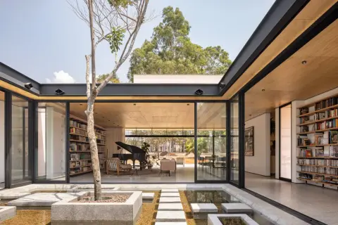 Modernas casas con patio interior central, un árbol solitario y un estanque de agua reflejan la luz natural.